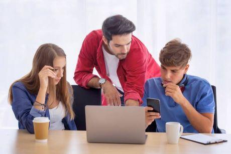 A man and his two friends in front of his laptop and phone, trying to figure out together which are the best 0% balance transfer credit cards.