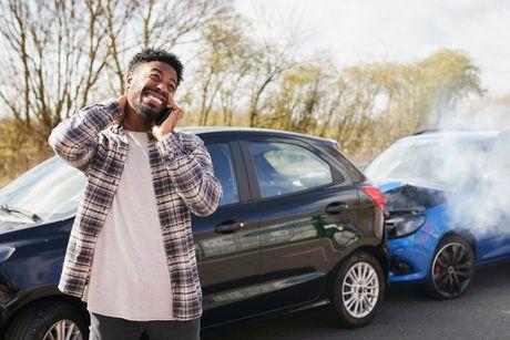 A man calling his car insurance company on a phone after his car got into an accident.