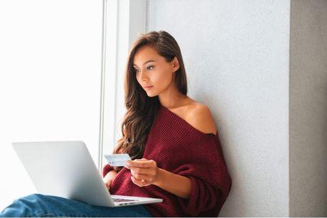 A young woman looking at her laptop and credit card, searching about the consequences for going over credit limit.