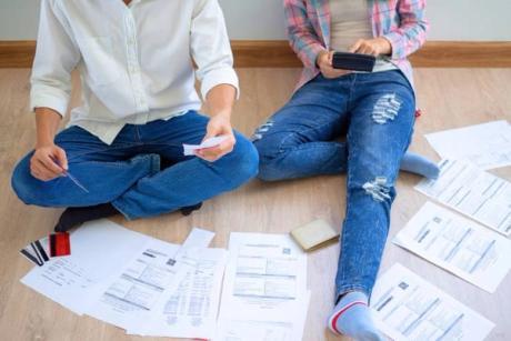 A couple sitting in down on the floor with a lot of documents and bills trying to figure out about Amigo Loans and how to find a guarantor for them.