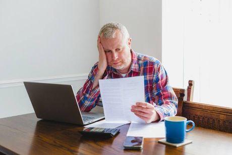 An old man looking very confused staring at his document and laptop screen, trying to figure out which bad credit loans have low interest rates.