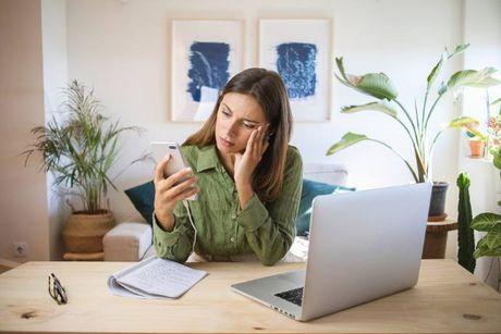 A woman sitting at her home in front of her laptop and using her phone to check why is she can't login to her ClearScore account.