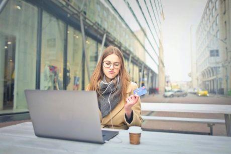 A girl in front of laptop holding a credit card, looking unhappy because the Argos credit card was shut down.