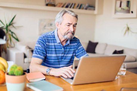 An old man sitting down in his living room and looking at his laptop searching for loans while having a CCJ.