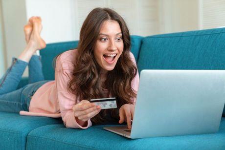 A young woman in her couch looking at her laptop very happily after applying for a credit card.