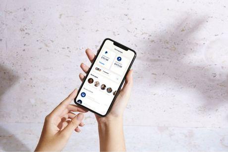 An image of someone holding a phone showing a PayPal homepage on the screen.