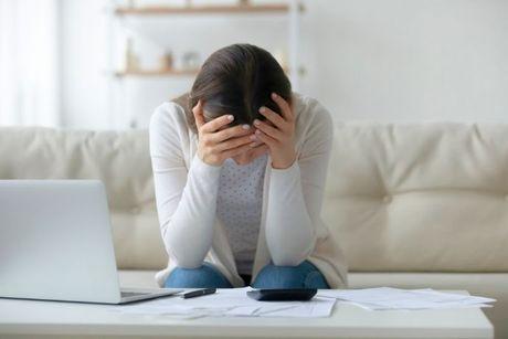 Young woman in front of a laptop and a stack of unpaid bills, worried about being in default.