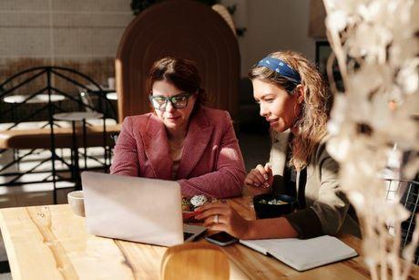 A young woman in front of a laptop explaining how credit score works to another woman.