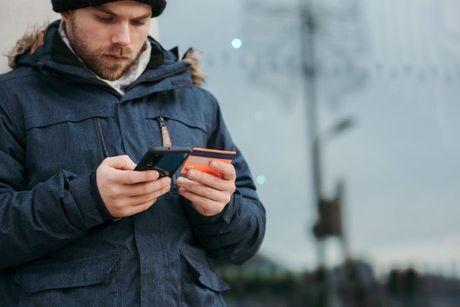 A guy looking at his credit card and his phone to search if a credit card is needed to build credit.