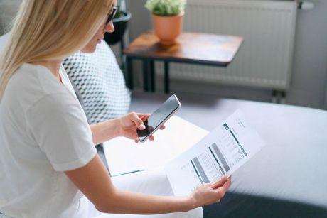 A woman looking at her bills documents and holding her phone to start paying her phone bills.