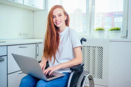 A young woman sitting at her wheelchair with her laptop on, figuring out how to get a loan if on benefits and bad credit.