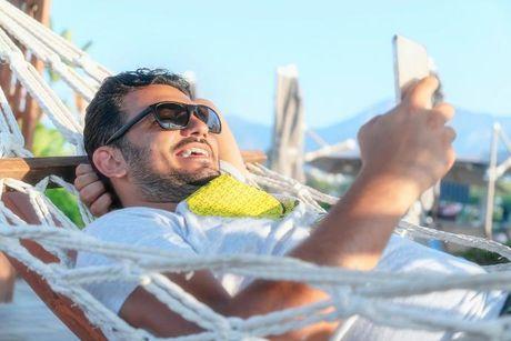 A man laying down on a hammock living abroad and looking at his phone figuring out how to get his UK credit report from abroad.