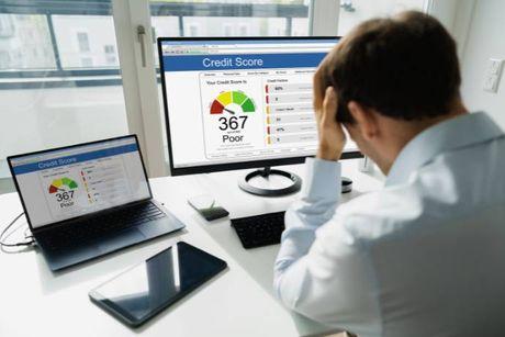 A man looking stressed in front of his computer, wondering why is his credit score going down and trying to figure out how to get it back up.