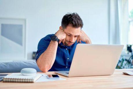 A man sitting down in his living room and looking at his laptop feeling stressed because his lender ignores his Notice of Correction.