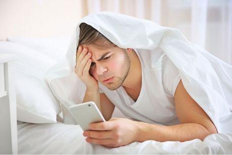 A man in his bed looking at his phone checking an update of his credit score.