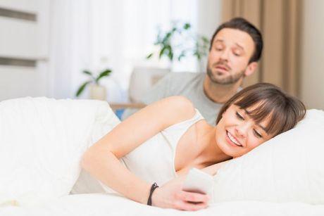 A couple in bed, with the husband trying to catch a glimpse of his wife's credit score on her phone.