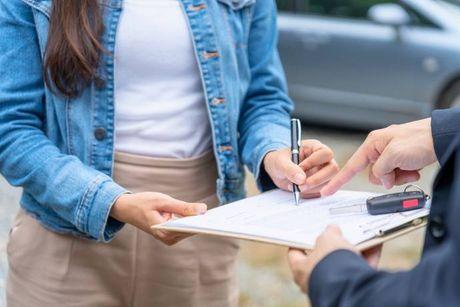 An image of a woman signing a document to lease a car.