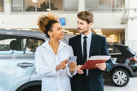 A young woman talking to a man working at a car dealer to ask how to get car finance with bad credit.