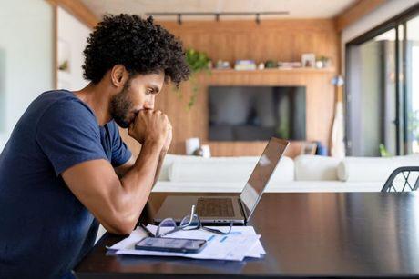 An image of man looking at his credit file on his laptop and worried about late payments.