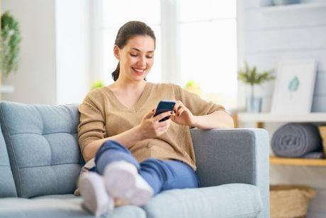 An image of woman sitting on her couch with her phone on her hands, searching an explanation about a good credit score.