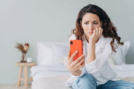 A young woman looking at her phone feeling confused and searching on the internet about how does an IVA affect credit score.