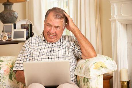 An old man looking very confused staring at his laptop screen trying to find his credit history from many years ago.