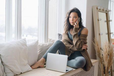 A girl sitting at her couch and looked annoyed calling Experian customer service on her phone.